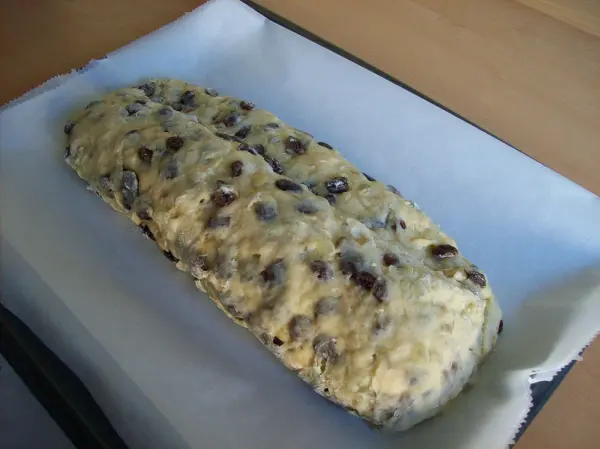 Ein frisch gebackener Christstollen liegt auf Backpapier und wartet auf das Verzieren mit Marzipan in einer hellen Küche.