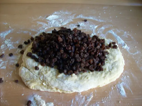 Ein unformierter Teig liegt auf einer bemehlten Oberfläche, während Trockenfrüchte darauf gestreut werden, bereit für die Zubereitung von Christstollen mit Marzipan.