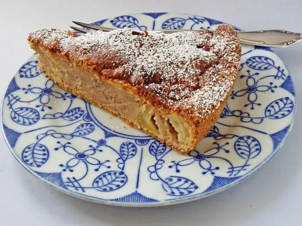 Ein Stück Apfel-Bananen-Kuchen ohne Zucker, verziert mit Puderzucker, liegt auf einem dekorativen Teller aus Porzellan.