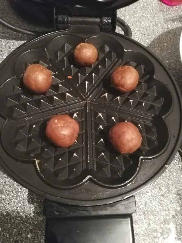 Runde Schoko-Teigkugeln liegen auf einem Waffeleisen, bereit zum Backen von Schoko-Zimtwaffeln in einer modernen Küche.