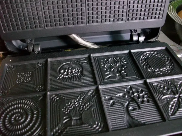 Eine Waffelmaschine mit dekorativen Formen steht bereit, um köstliche Schoko-Zimtwaffeln zu backen.
