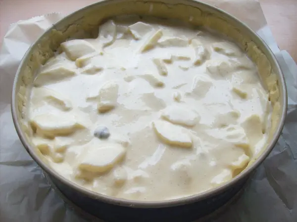 Ein Käse-Apfel-Kuchen in einer runden Backform, gefüllt mit einer cremigen Mischung und Apfelstückchen, wartet auf das Backen.