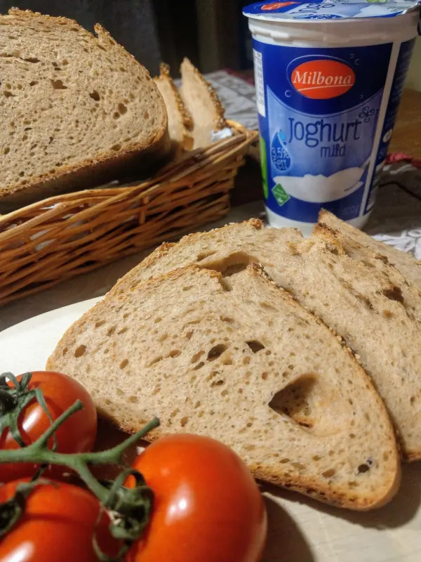 Schnitzel aus Vollkornbrot liegt neben Joghurt und frischen Tomaten auf einem Holzbrett in einer rustikalen Küche.