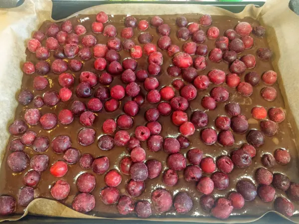 Eine Mischung aus Schokoladenmasse wird mit zahlreichen roten Kirschen bedeckt, um einen Schwarzwälder Käsekuchen zu kreieren.