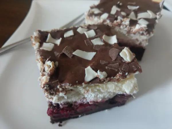 Zwei Stücke Schwarzwälder Käsekuchen liegen auf einem weißen Teller, dekoriert mit Schokoladenstücken und Sahne.