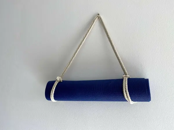 Eine blaue Yogamatte ist mit einem Seil aufgehängt, das sie sicher zusammenhält, vor einer hellen Wand.
