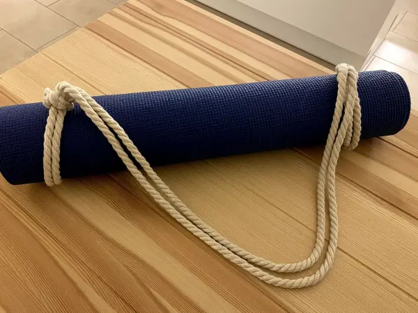 Ein blauer Yoga- und Sportmatten-Roll mit einem selbstgemachten, geflochtenen Tragegurt liegt auf einem Holztisch.