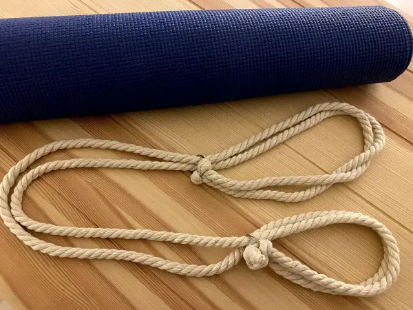 Ein blauer Yogamatte liegt auf einem Holzuntergrund, daneben liegt ein selbstgemachter Tragegurt aus dicken, hellen Schnüren.