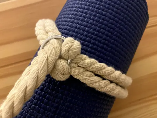 Ein geknoteter Tragegurt aus natürlichem Material hält eine dunkelblaue Yogamatte zusammen, auf einer Holzoberfläche.