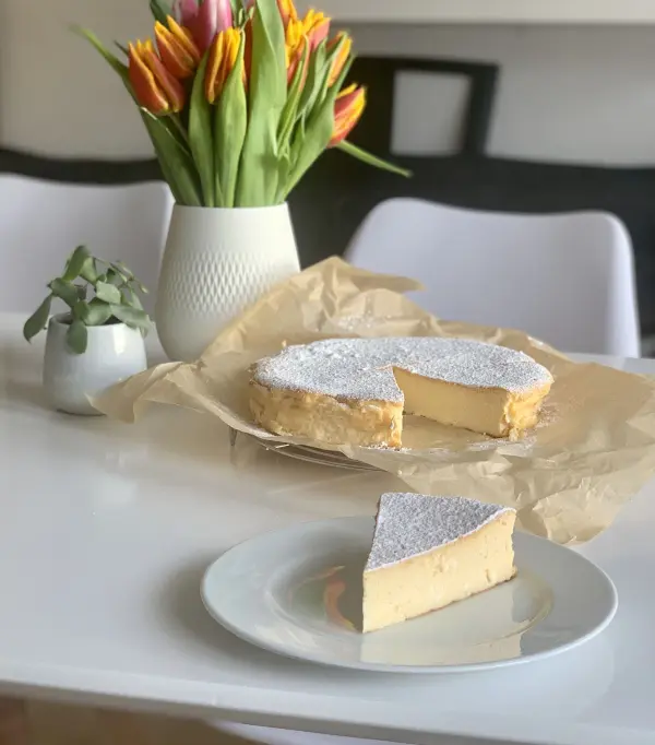 Ein leckerer Käsekuchen ohne Boden steht auf einem Tisch, umgeben von frischen Blumen und einem kleinen Pflanzenarrangement.