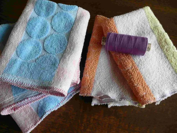 Bunte Frottee-Handtücher liegen auf einem Tisch, während eine lila Nähgarnrolle daneben darauf wartet, verwendet zu werden.