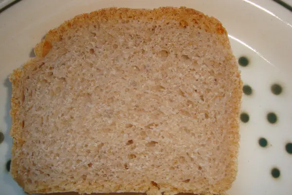 Ein Stück Dinkelbrot liegt auf einem Teller mit grünen Punkten, frisch geschnitten und bereit zum Verzehr.