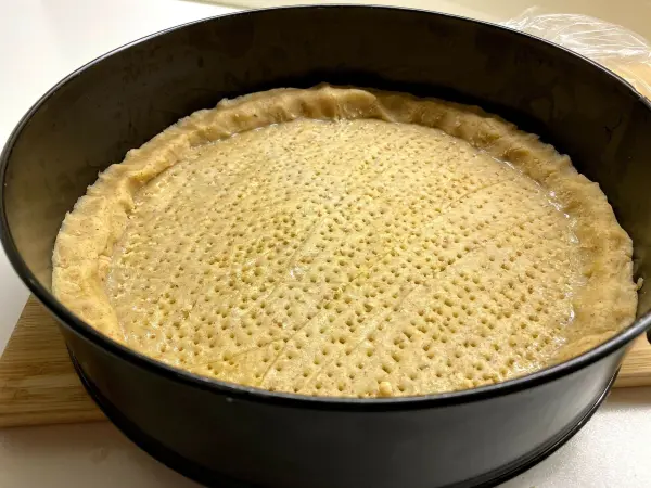 Ein runder, ungebackener Torta della Nonna-Boden liegt in einer Springform und zeigt eine gleichmäßige, gepickte Oberfläche.