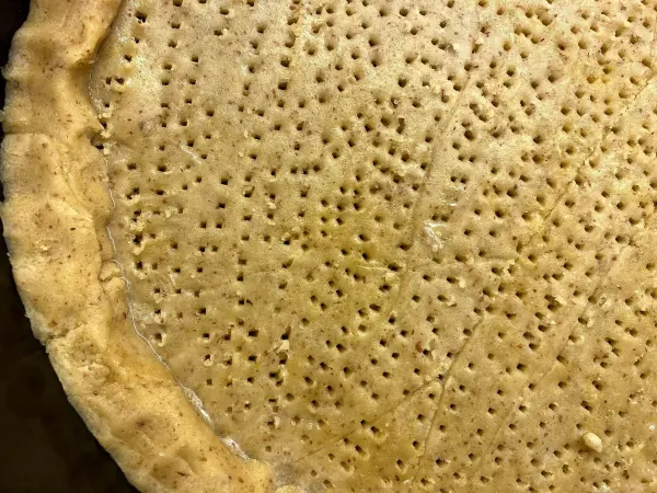 Ein gebräunter Torta della Nonna-Boden liegt flach auf einem Blech, mit gleichmäßigen Löchern für das Backen.