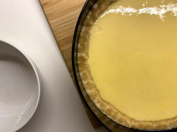 Ein Tortenboden wird mit einer gelben Füllung für Torta della Nonna vorbereitet, platziert auf einer Holzunterlage.