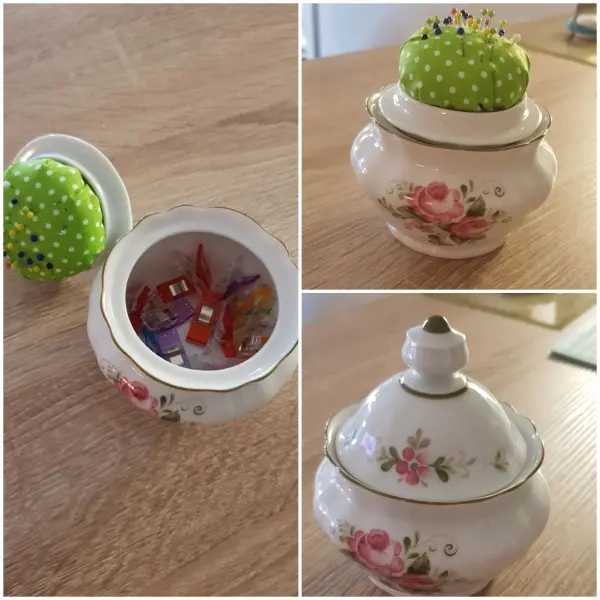 Ein dekoratives Nadelkissen aus einem grünen gepunkteten Stoff sitzt auf einem Keramikgefäß mit Blumenmuster.