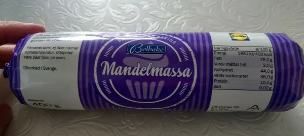 Eine Rolle Mandelmassa mit lila Verpackung wird gehalten. Sie ist für die Herstellung von süßen Backwaren gedacht.