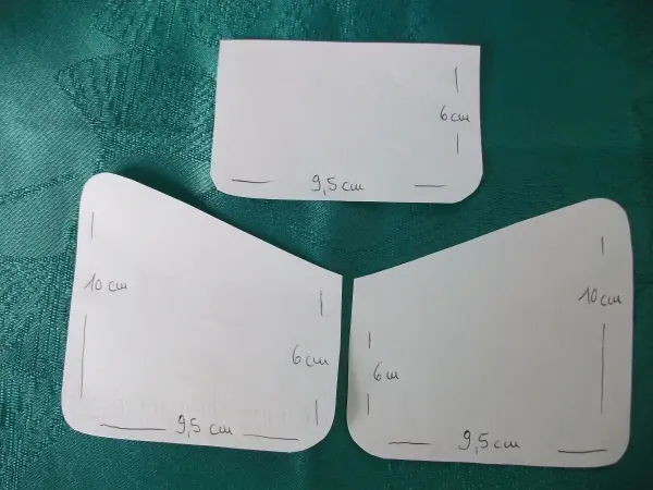 Drei Papierzuschnitte für kleine Geldtaschen liegen auf einem grünen Tisch und zeigen Maßangaben in Zentimetern.