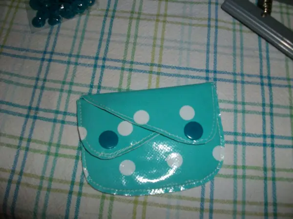 Eine kleine, türkisfarbene Geldtasche mit weißen Punkten liegt auf einem karierten Tischcloth.