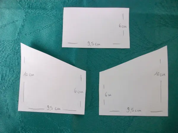 Drei Papierzuschnitte für das Nähen von kleinen Geldtaschen liegen auf einem grünen Stoff. Maße sind deutlich sichtbar.