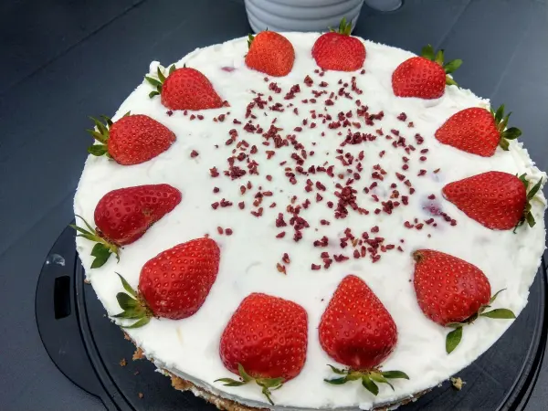 Eine Erdbeertorte mit Frischkäse liegt auf einem gedeckten Tisch, dekoriert mit frischen Erdbeeren und Schokoladenstückchen.
