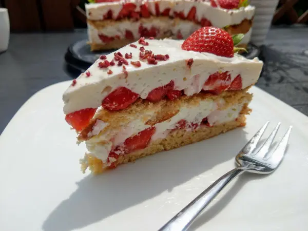 Eine saftige Erdbeertorte mit Frischkäse ruht auf einem weißen Teller, während ein Stück davon bereits herausgeschnitten ist.