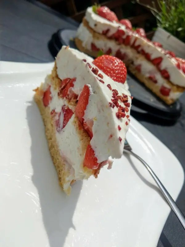 Eine frische Erdbeertorte mit Frischkäse steht auf einem weißen Teller, während ein Stück dekoriert mit Erdbeeren hervorsticht.