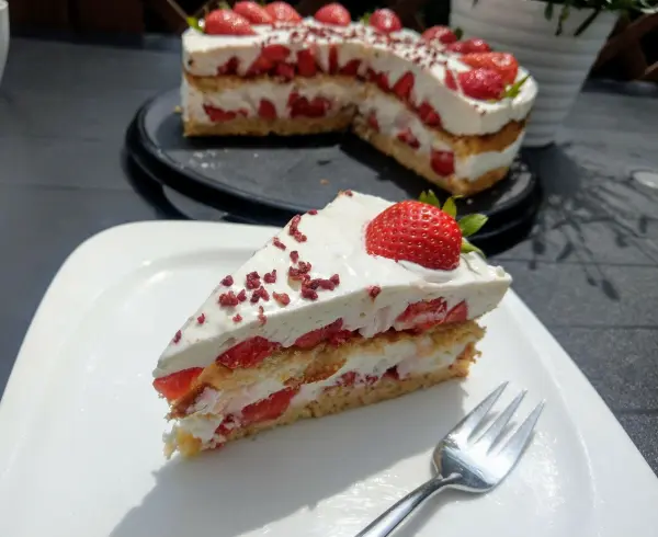 Eine saftige Erdbeertorte mit Frischkäse und Schlagsahne, dekoriert mit frischen Erdbeeren, steht auf einem Teller.