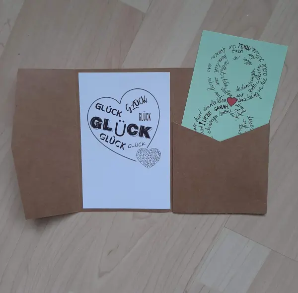 Eine Glückwunschkarte zeigt viele "Glück"-Worte, die in einem Herz angeordnet sind, zusammen mit einer persönlichen Nachricht.