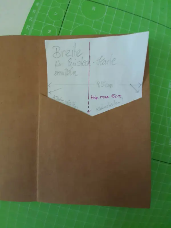 Eine braune Karte zeigt eine Skizze zur Breite einer Glückwunschkarte mit Maßen für die Anfertigung auf grünem Untergrund.