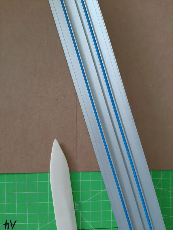 Drei gerade Linien aus Kunststoff liegen auf braunem Karton, während ein Knickwerkzeug bereit ist, um eine Karte zu gestalten.
