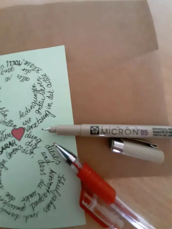 Eine handgeschriebene Karte zur Versetzung liegt auf einem Tisch, umgeben von Stiften und einem beige Hintergrund.