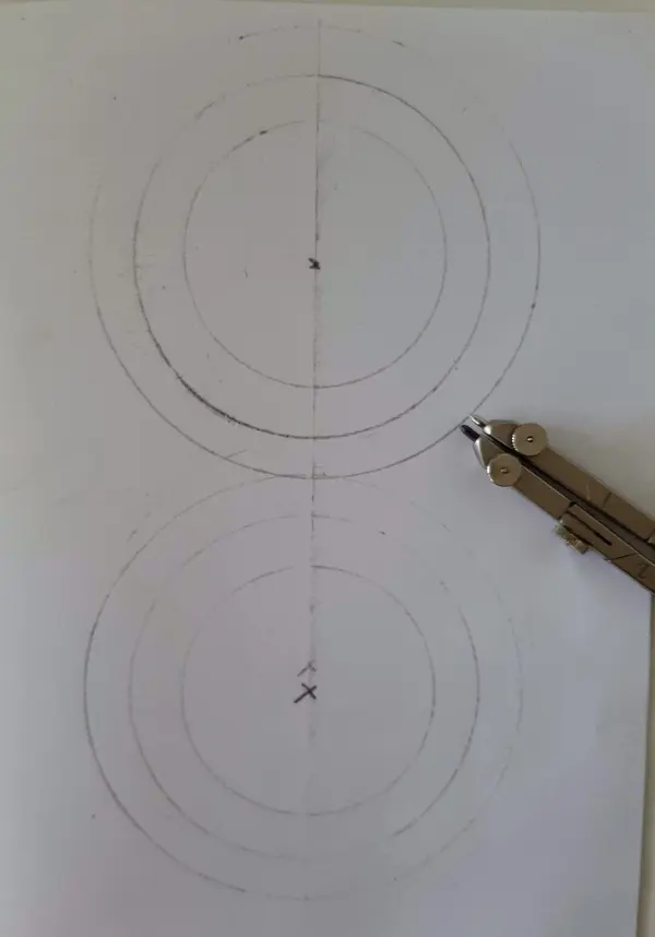 Zwei konzentrische Kreise werden mit einem Zirkel auf ein Blatt Papier gezeichnet, um geometrische Formen zu erstellen.