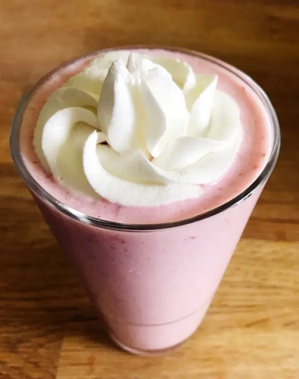 Ein Erdbeer-Bananen-Milchshake in einem Glas, garniert mit Sahne, steht auf einem Holztisch.