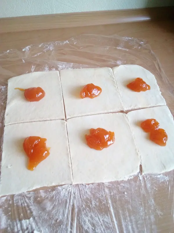 Sechs Teigstücke liegen nebeneinander, jeweils mit einem Klecks Quark gefüllt, auf einer Arbeitsfläche.