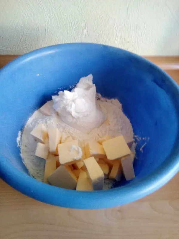 In einer blauen Schüssel befinden sich Quark und Butterwürfel auf Mehl, bereit zum Mischen für Quark-Kissen.