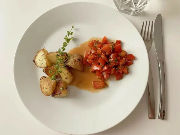 Auf einem weißen Teller liegen gebratene Kartoffeln und frisches Paprikagemüse in einer Sauce, garniert mit Kräutern.