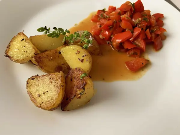Eingebratenen Kartoffeln liegen neben frisch gehacktem Paprikagemüse auf einem weißen Teller, appetitlich angerichtet.