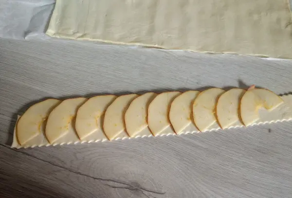 Apfelrosen werden zubereitet, indem dünne Apfelscheiben auf einen ausgerollten Teig gelegt werden, auf einem hellen Tisch.