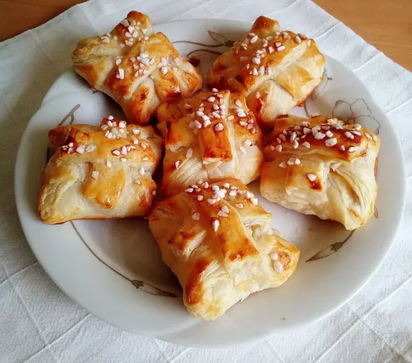 Sechs goldbraune Blätterteig-Quark-Teilchen ruhen auf einem weißen Teller, bestreut mit feinem Zucker.