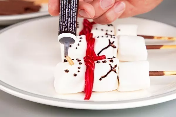 Mit Lebensmittelfarbe oder Schokosoße zauberst du deinen Marshmallow-Schneemännern ein Gesicht.