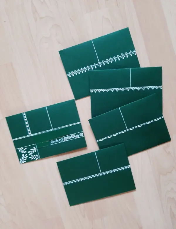 Fünf grüne Weihnachtskarten liegen auf einem hellen Holztisch und zeigen einfache, dekorative Faltungen und Muster.
