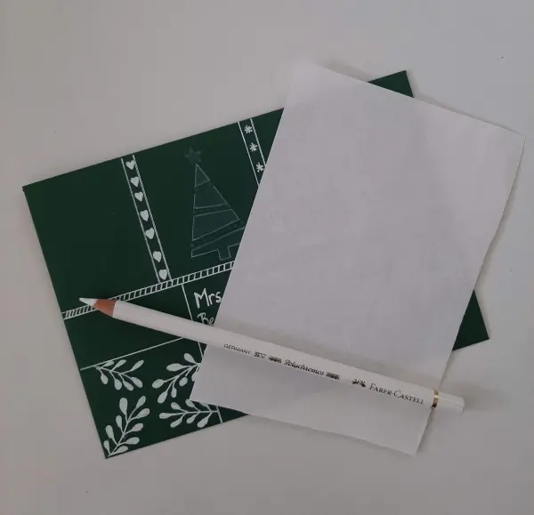 Eine grüne Weihnachtskarte mit einem gefalteten Tannenbaum liegt neben einem weißen Bogen Papier und einem Bleistift.