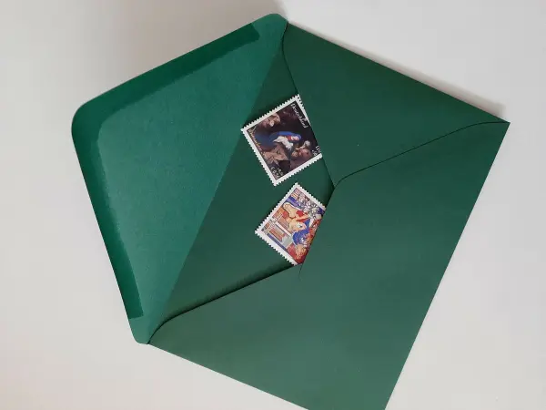Eine grüne Weihnachtskarte liegt offen mit zwei traditionellen Briefmarken sichtbar, um den festlichen Inhalt anzudeuten.
