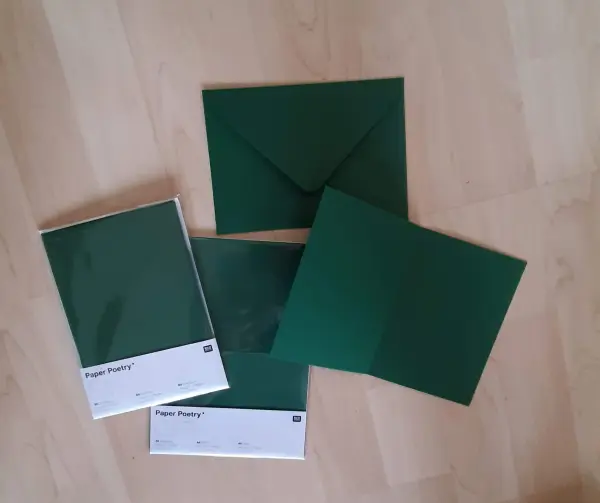 Eine grüne Weihnachtskarte mit einem gefalteten Tannenbaum liegt auf einem hellen Holzuntergrund, umgeben von Umschlägen.