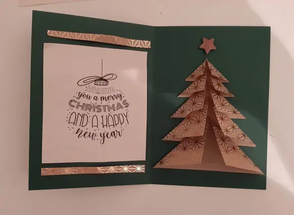 Eine grüne Weihnachtskarte zeigt einen gefalteten Tannenbaum aus goldenem Papier und einen Weihnachtsgruß.
