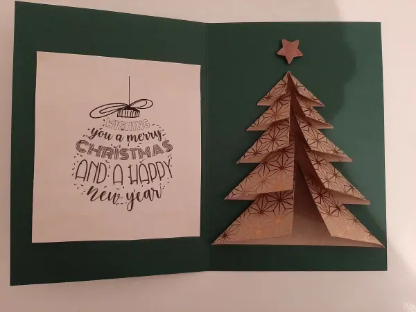 Ein gefalteter Tannenbaum steht auf einer grünen Karte, die eine Weihnachtsbotschaft enthält: „Wishing you a merry Christmas and a happy New Year.“