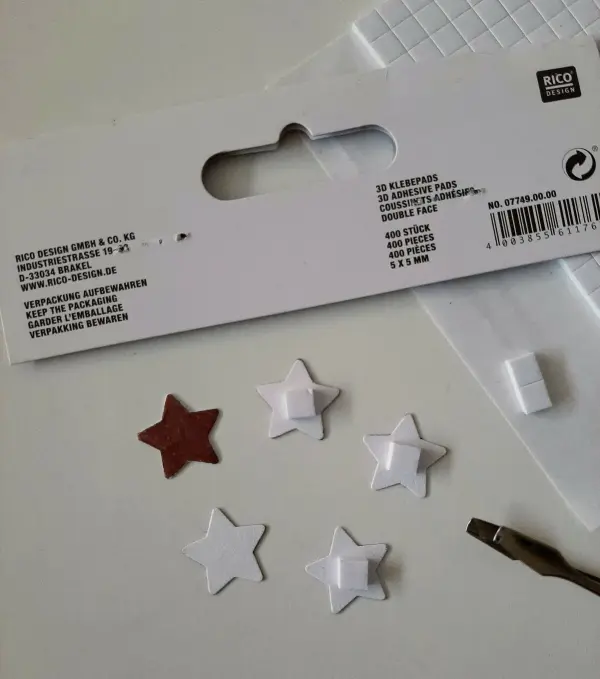 Eine Packung mit 3D-Klebe-Elementen in Sternform liegt auf einem Tisch, bereit für kreatives Gestalten von Weihnachtskarten.