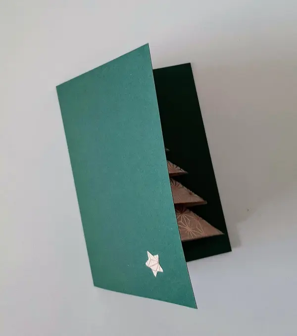 Eine grüne Weihnachtskarte ist geöffnet, zeigt einen gefalteten Tannenbaum im Inneren und einen kleinen Stern außen.