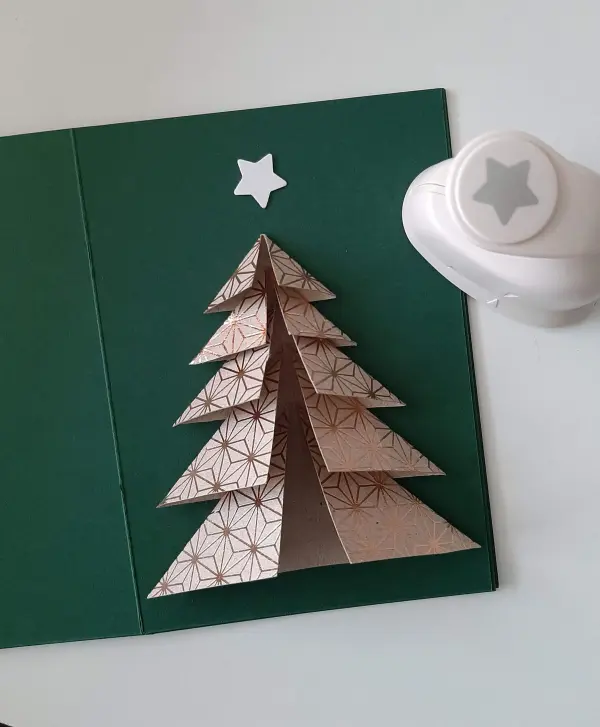 Ein gefalteter Tannenbaum steht dreidimensional auf einer grünen Karte, daneben befindet sich ein Sternenlocher.
